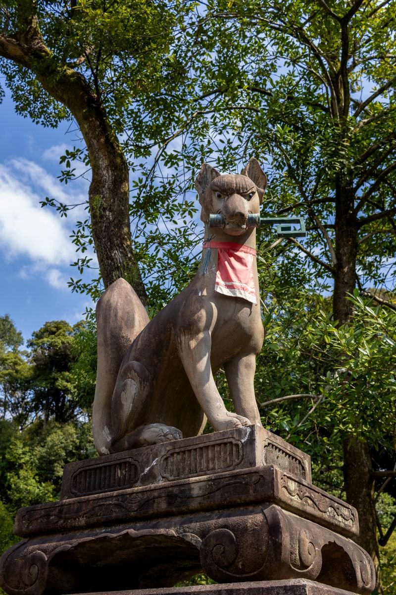 Stone fox guardian statue with a red bib at a Japanese Inari shrine