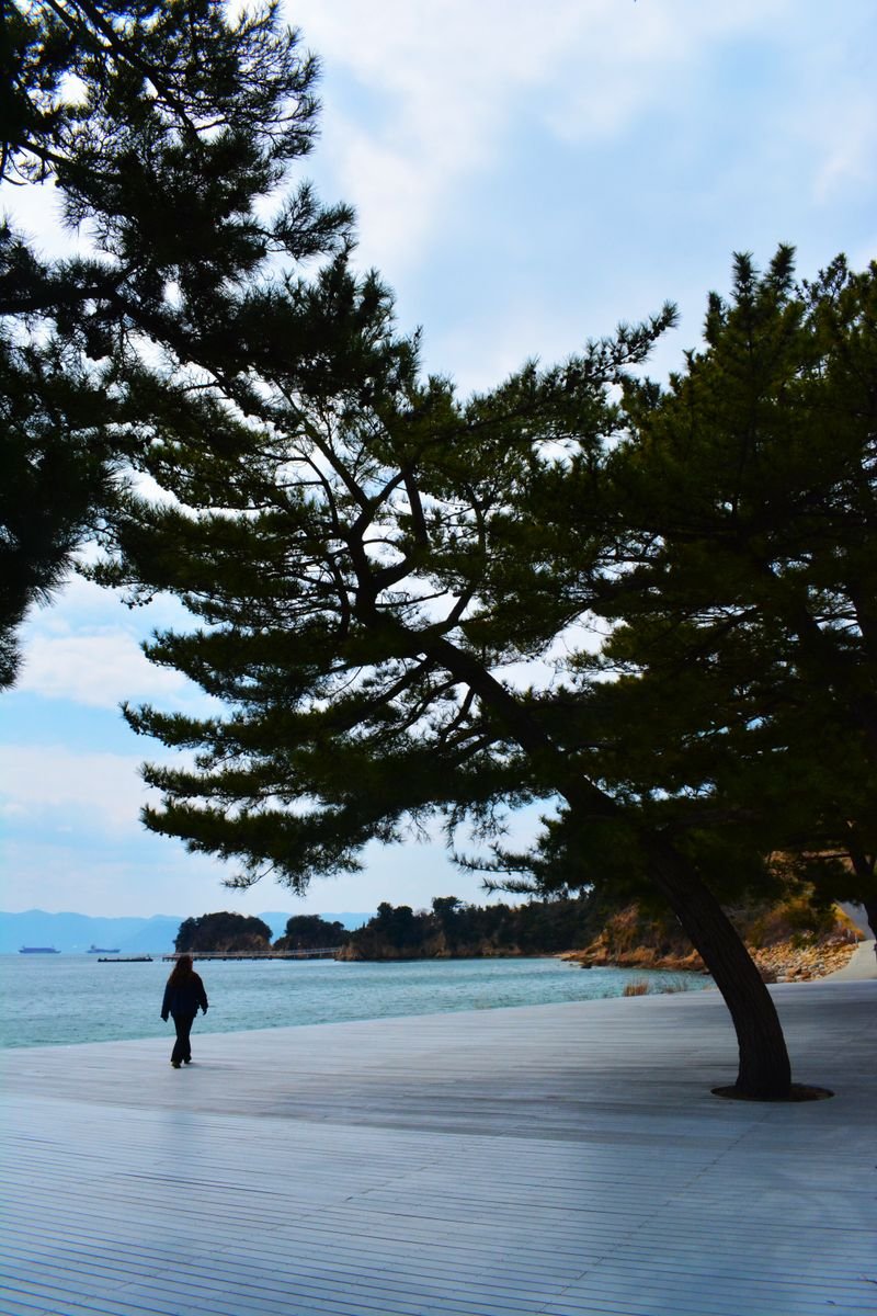 A lone figure walks along the seaside promenade in Naoshima, Kagawa, Japan.