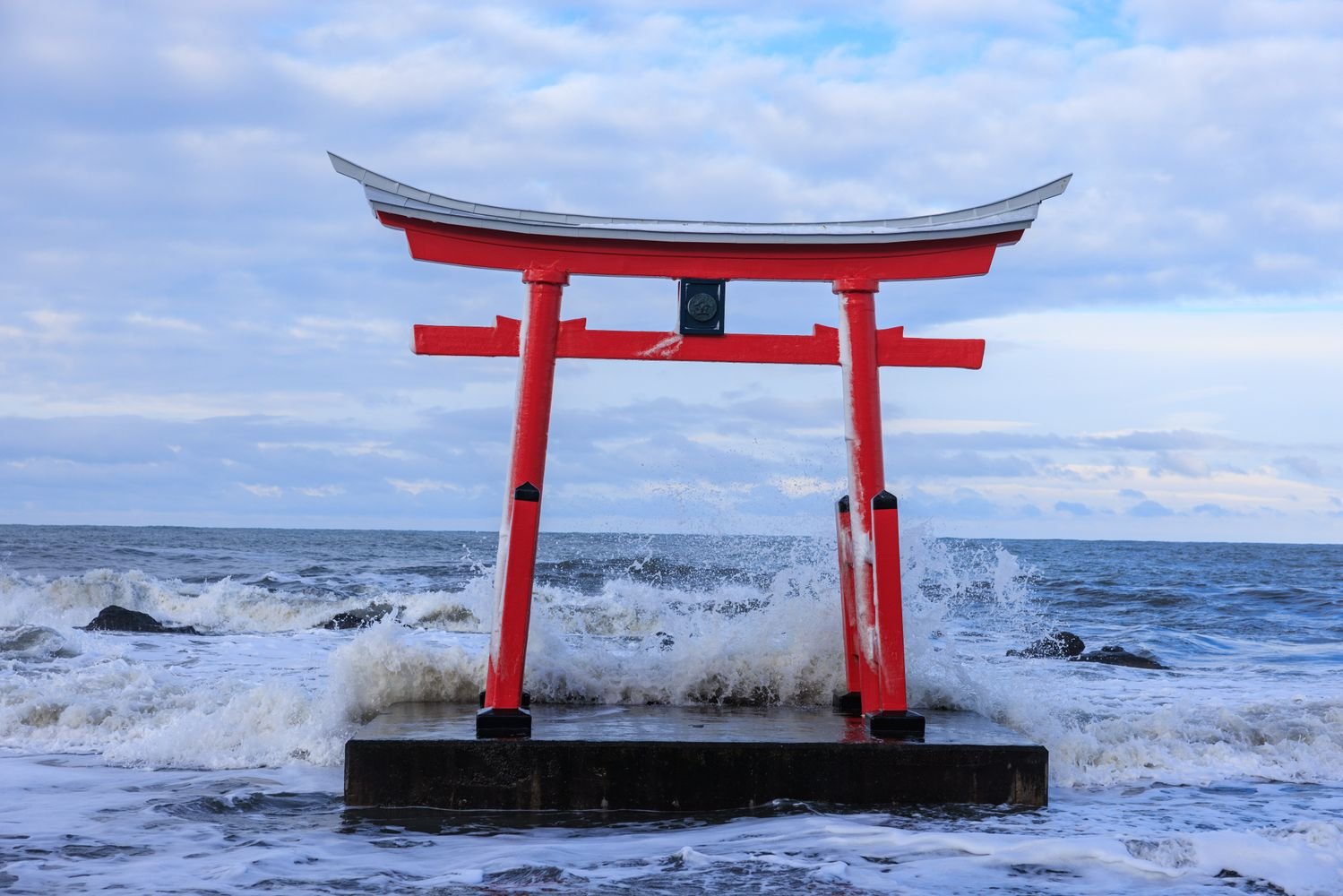 Red torii gate standing in the ocean with waves crashing around it