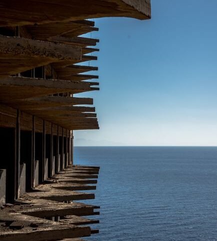 Weathered concrete building overlooking the sea, evocative of Gunkanjima / Hashima Island's ruins
