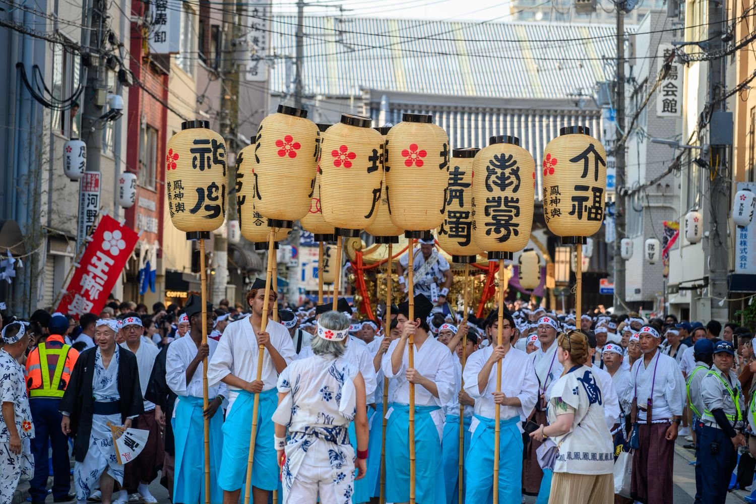 Men in traditional happi coats carrying lanterns on poles during a Japanese festival procession