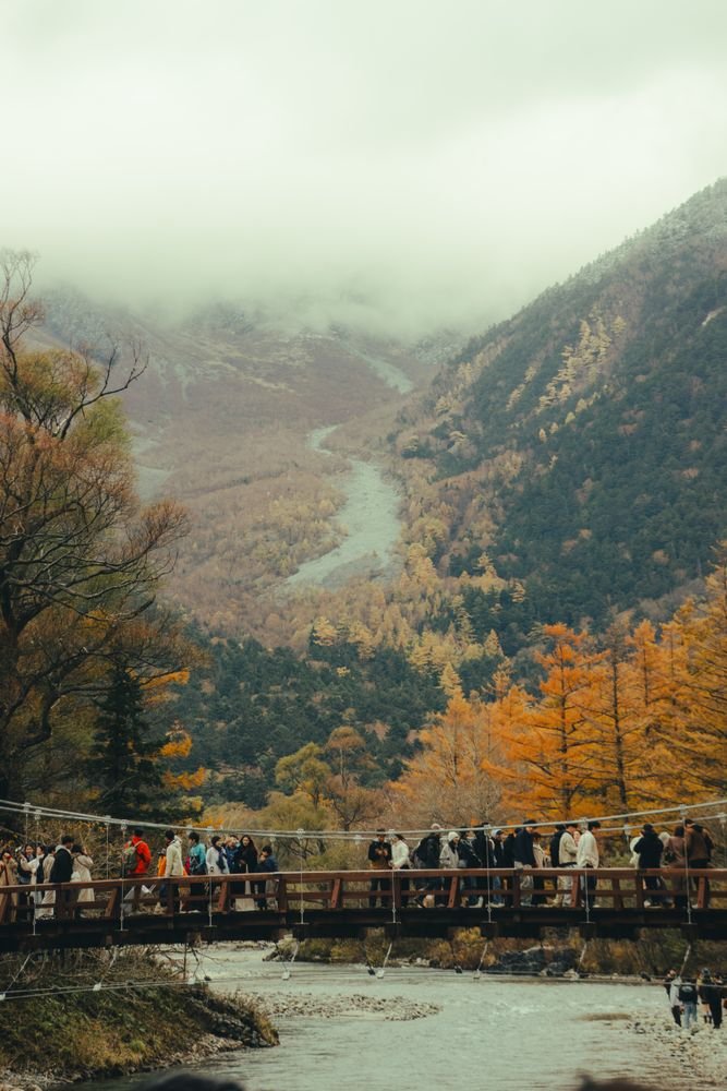 A wooden suspension bridge over a river with mountains in the background in Nagano, Japan