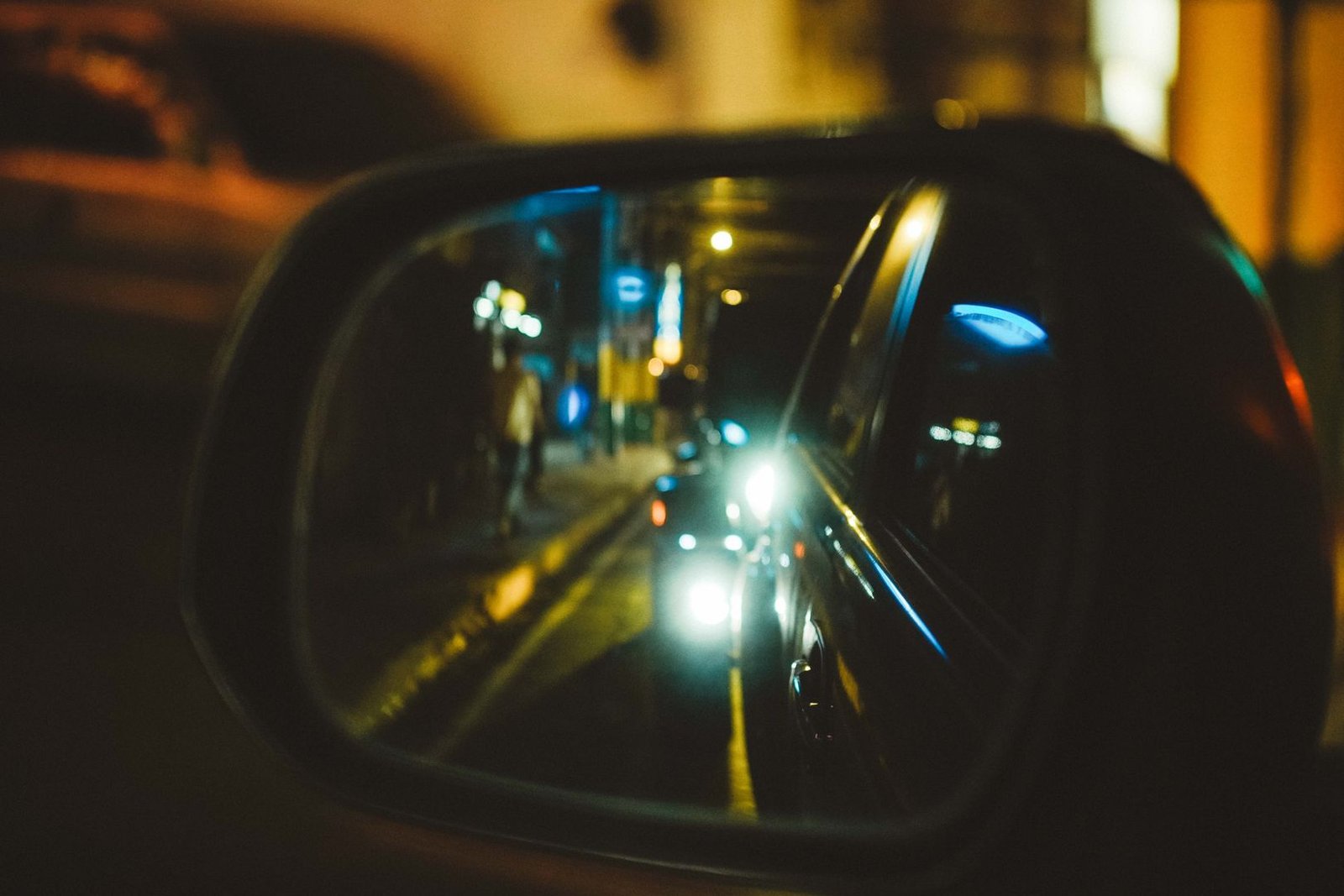 A car's side mirror reflecting city lights at night, evoking the tunnel's mirror-related ghost legends