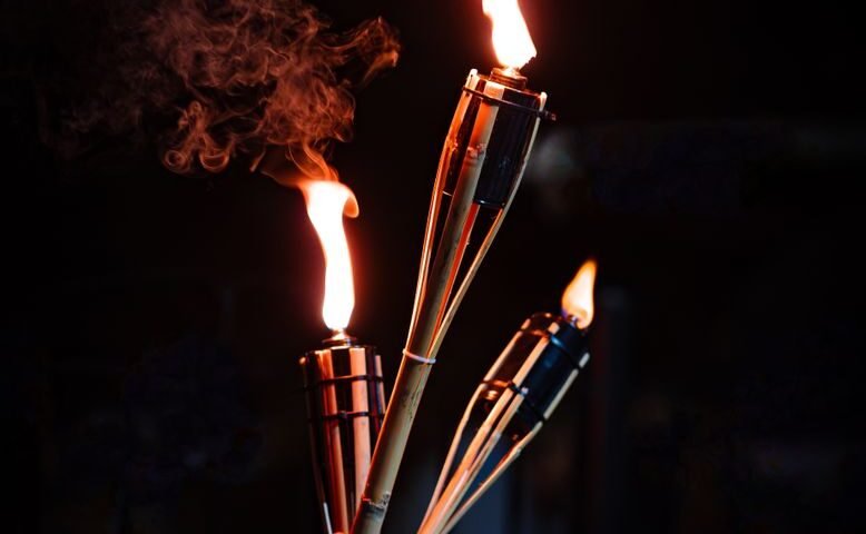 Flaming torches held aloft at night, evoking the huge pine torches carried through Kurama during the fire festival