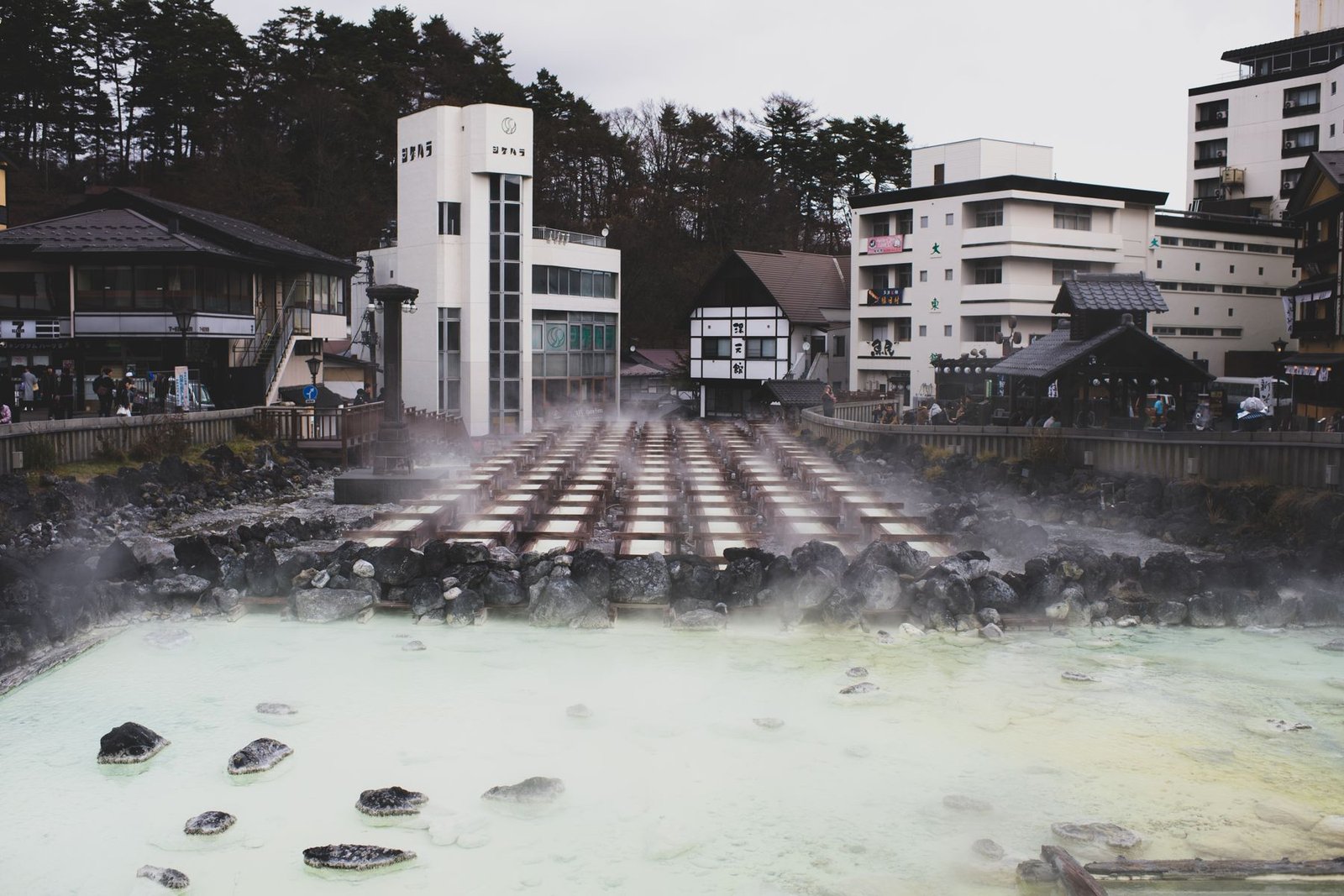 A tranquil hot spring town with steam rising from mineral-rich waters, surrounded by traditional architecture