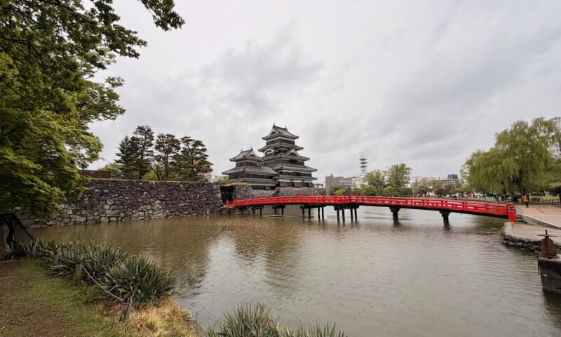 Matsumoto Castle tower reflected near a red bridge in spring
