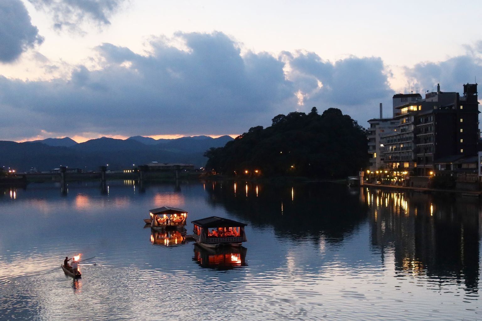 A calm river at dusk in Japan, with hills in the background