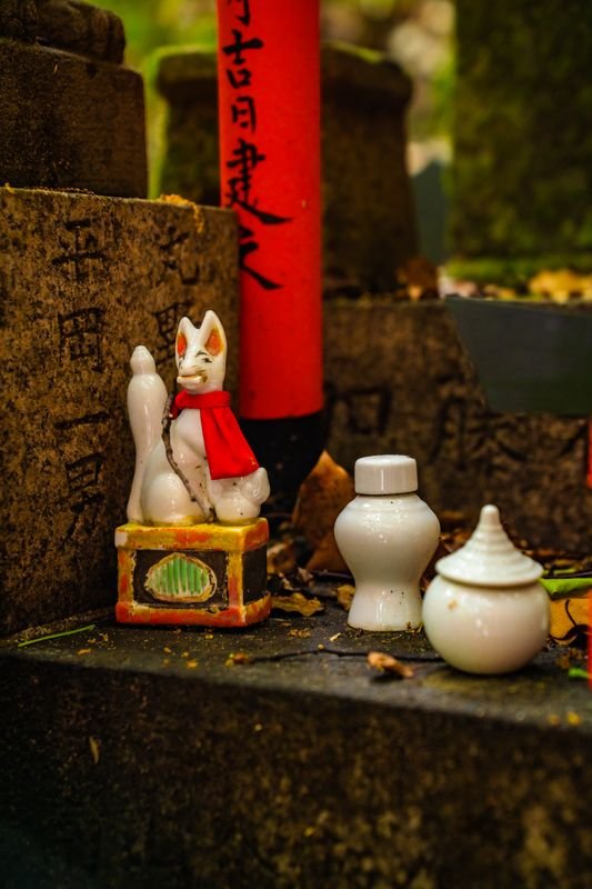 Ceramic fox statue with traditional offerings at a Japanese Inari shrine