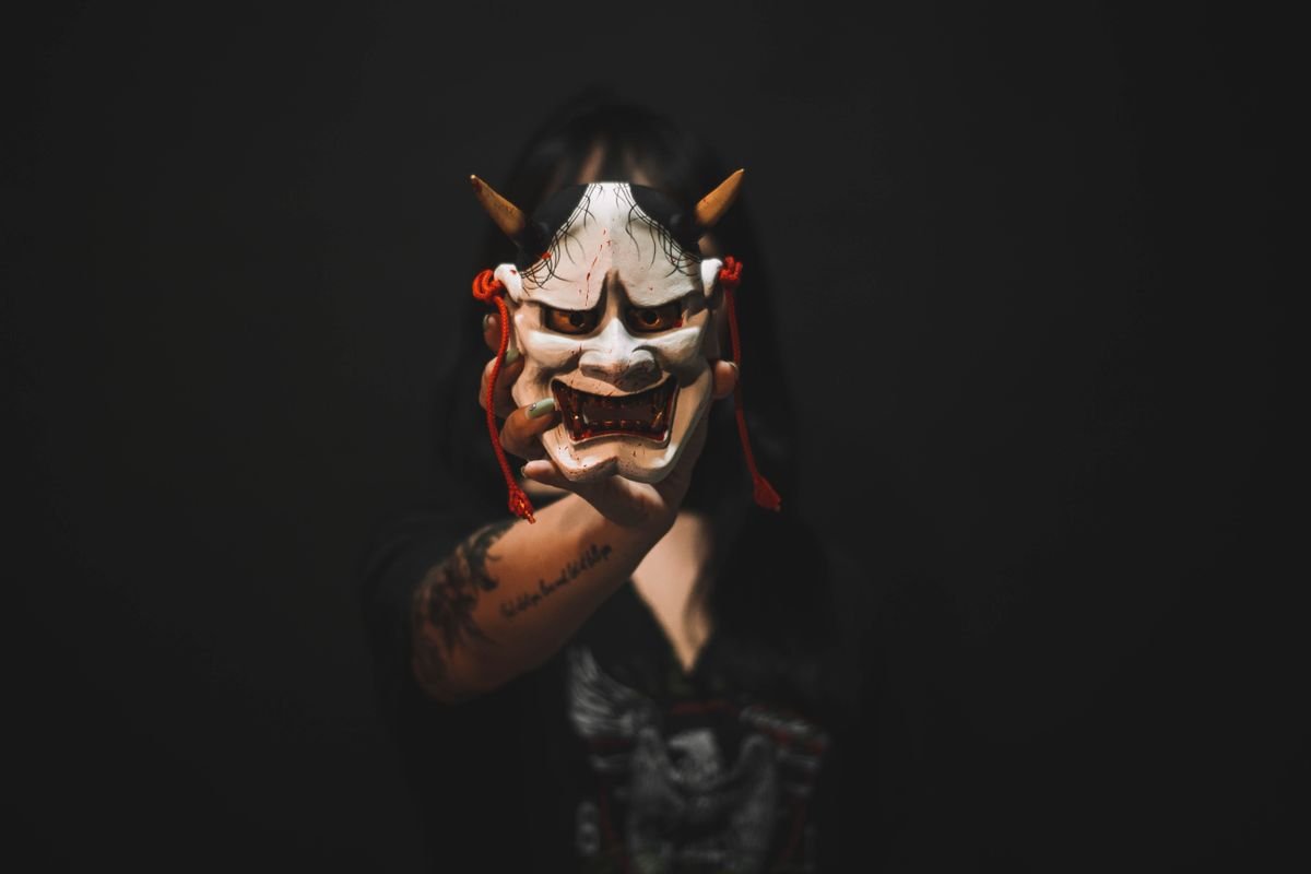A traditional Japanese demon mask held up against a dark background