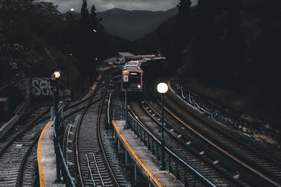 A train approaching a dimly lit station at night surrounded by mountains, illustrative stock photo