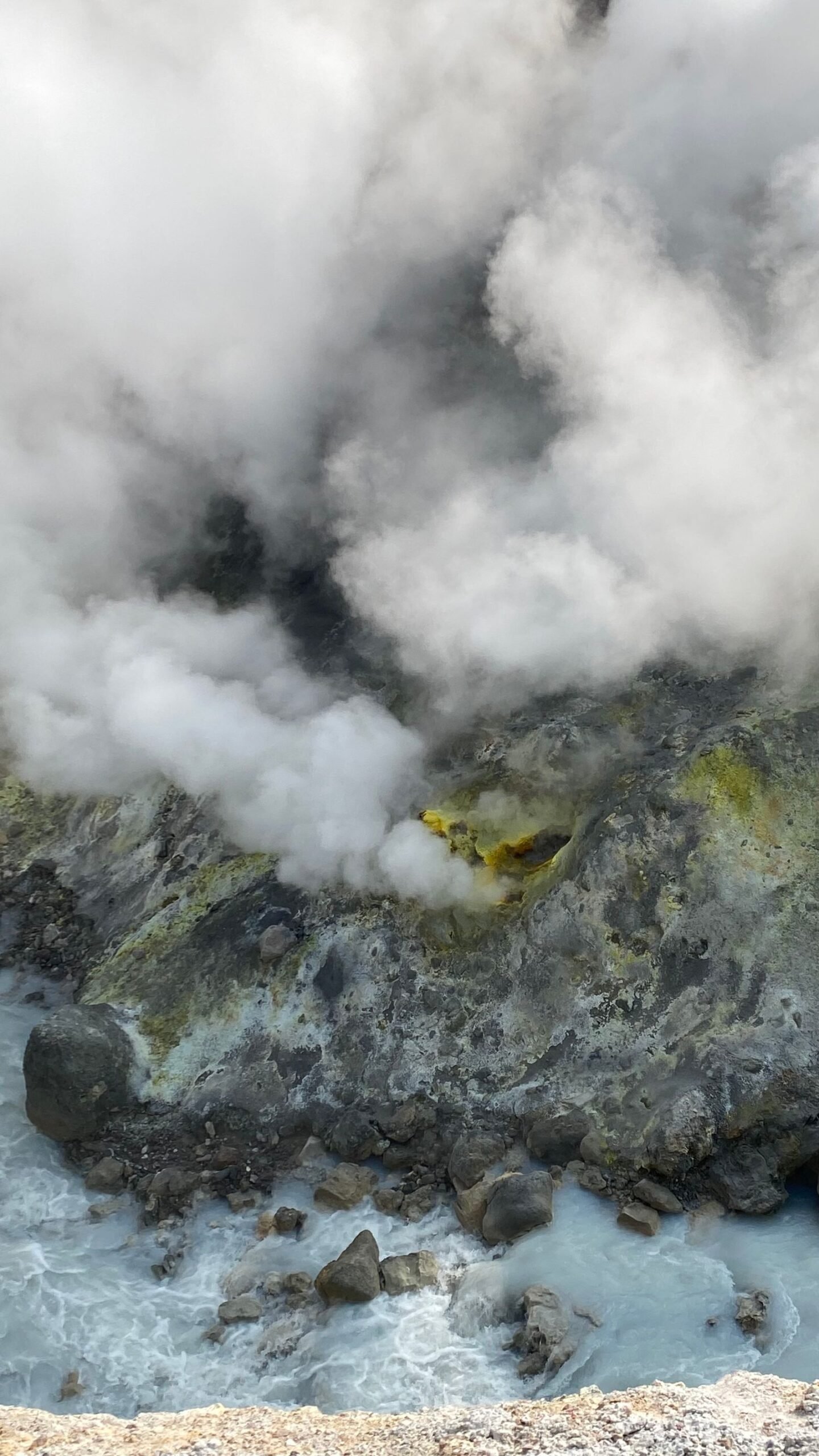 Sulfur-yellowed volcanic hot spring with steam rising off bubbling water